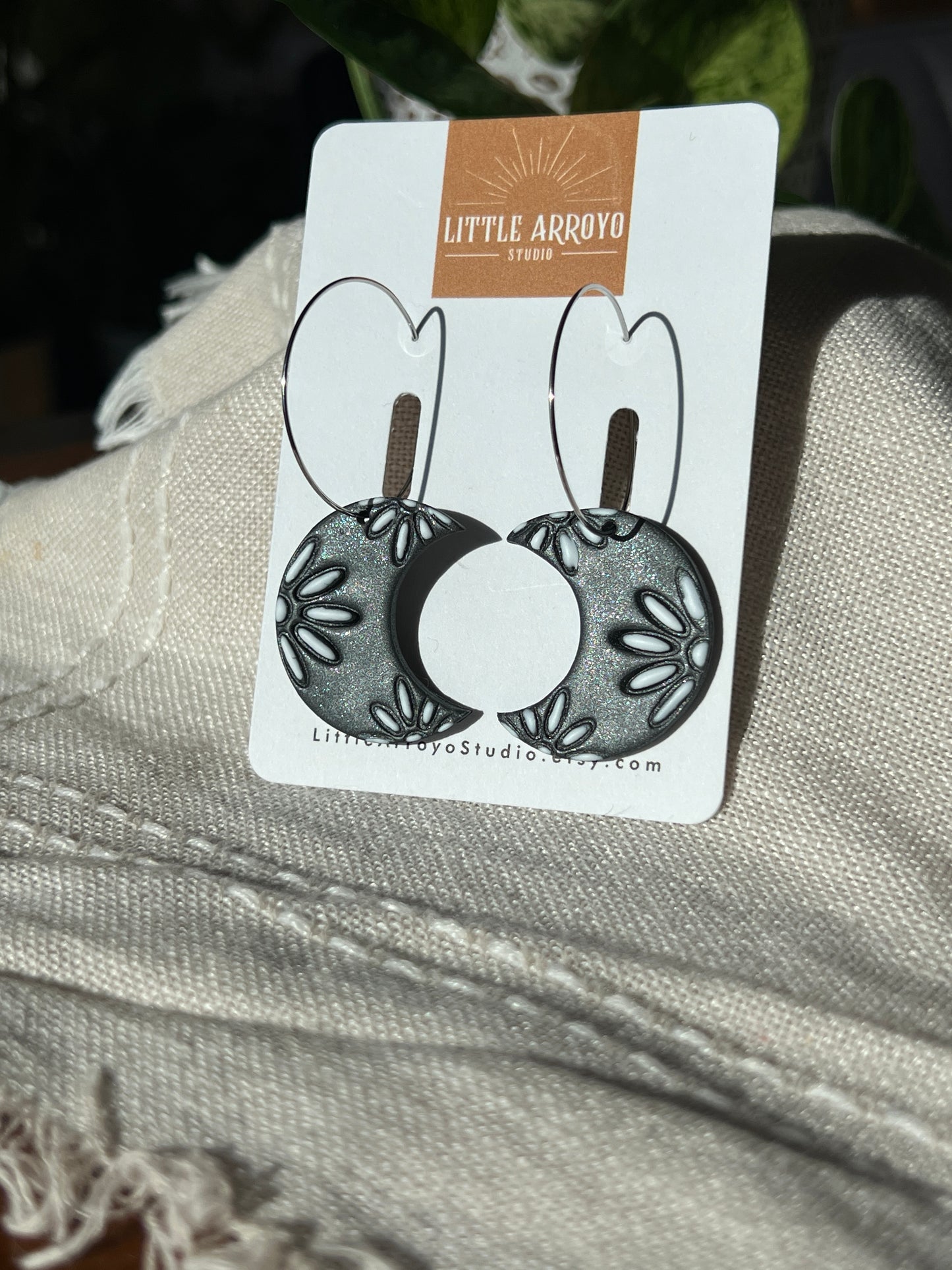 Sparkly, oversized floral moon earrings on a card with 'Little Arrow Studio' branding, displayed on a textured fabric background. Handmade polymer clay lightweight hypoallergenic