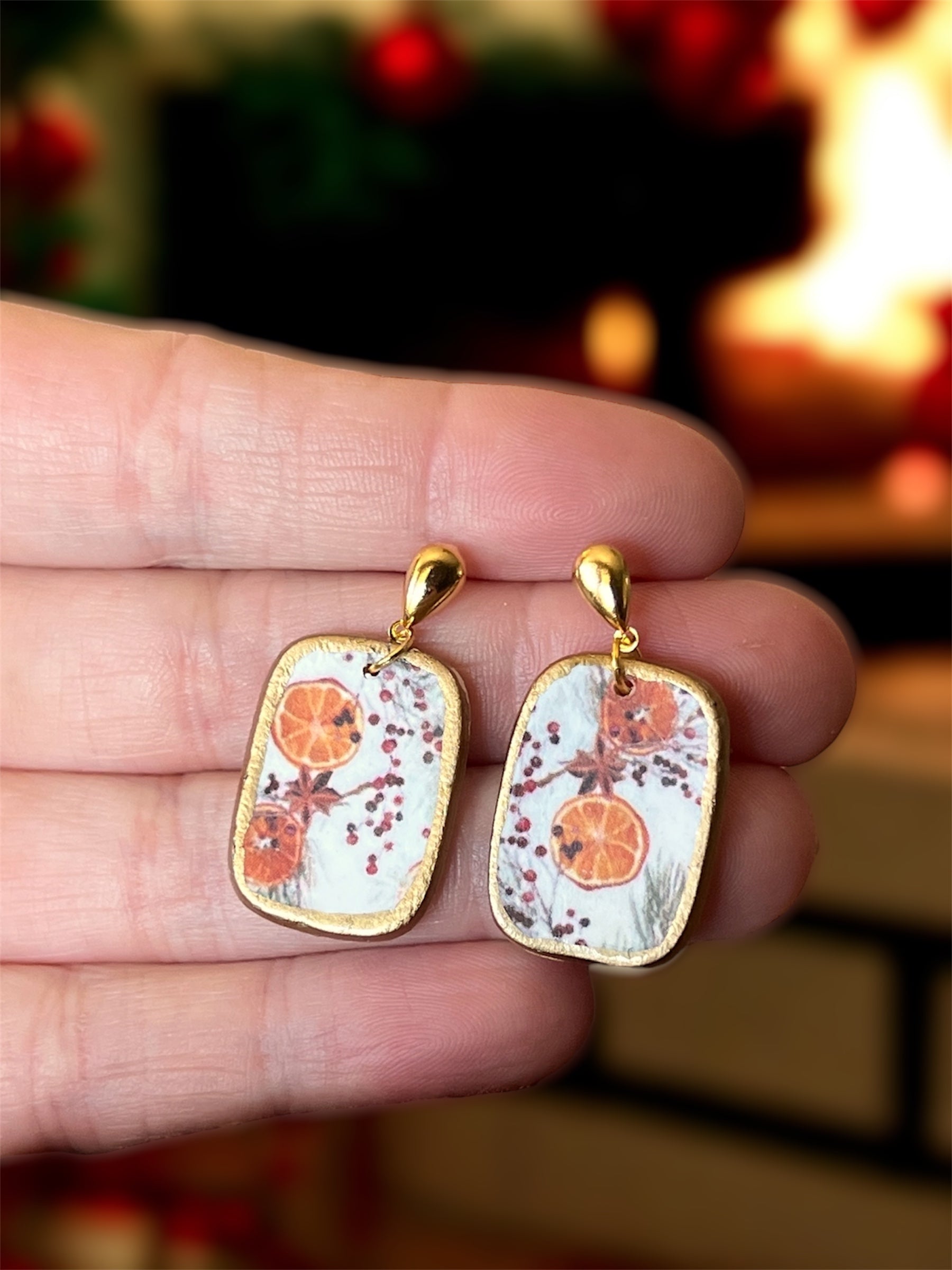 Decorative fall Thanksgiving winter potpourri earrings, handmade polymer clay lightweight hypoallergenic, held between fingers with a blurred background
