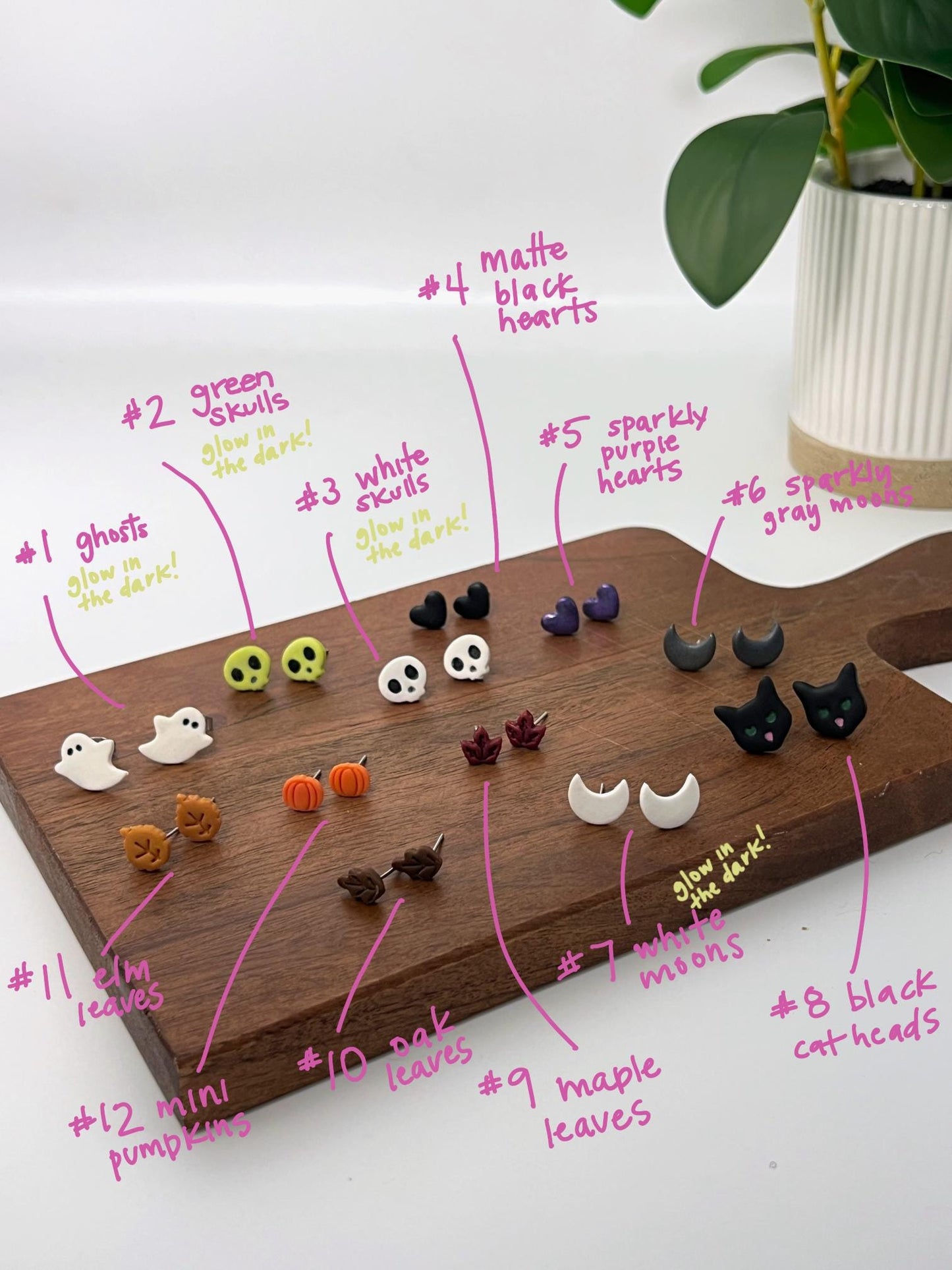 Wooden board with various small handmade polymer clay hypoallergenic Halloween earrings labeled on a white surface.